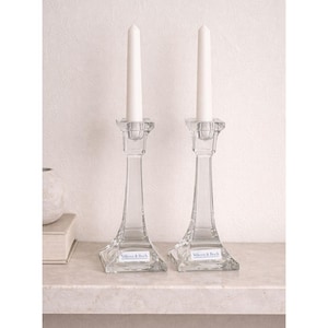 May include: Two clear glass candle holders with white candles. The candle holders have a square base and a tall, slender stem. Each base has a label reading "Villeroy & Boch".
