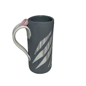 May include: A tall, gray ceramic mug with a white handle and a pink accent. The mug features a design of angled stripes in white, yellow, and blue. The mug is designed for hot beverages.