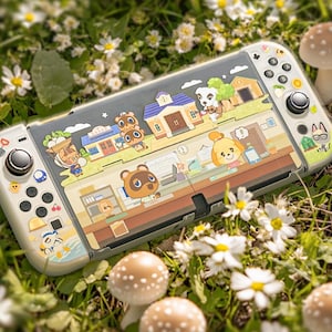 May include: A Nintendo Switch console with an Animal Crossing theme. The white Joy-Cons have themed buttons, and the screen cover displays a colourful village scene with cartoon characters. The console is set on grass, daisies, and mushrooms.