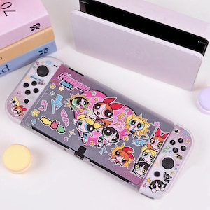 Puede incluir: Una funda protectora transparente para una consola Nintendo Switch, con un diseño de los personajes de las Supernenas. La funda tiene un fondo gris con detalles en rosa y gráficos de dibujos animados coloridos. Se ven la consola Switch y la base.