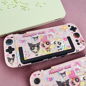 May include: Pink Nintendo Switch Joy-Con controllers with a Powerpuff Girls design. The controllers feature cartoon characters, hearts, bows, and rainbows. The text "Powerpuff Girls" is printed on the controllers.