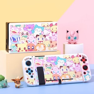 Könnte beinhalten: Weißes Nintendo Switch Konsolen- und Dockingstation-Set mit einem farbenfrohen Cartoon-Charakter-Design. Das Design zeigt verschiedene Charaktere in Rosa-, Gelb-, Blau- und Lilatönen. Eine rosa Figur eines Charakters ist ebenfalls vorhanden.
