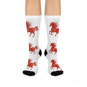 May include: White socks with a repeating pattern of red horses with gold accents. The horses are depicted in a running pose with flowing manes and tails. The socks have black heels and toes.
