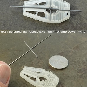May include: A transparent plastic mast building jig, featuring slots and openings. The image shows the jig with mast wire and a coin for size comparison. Text on the image reads "WTJ NAVAL | MAST BUILDING JIG".