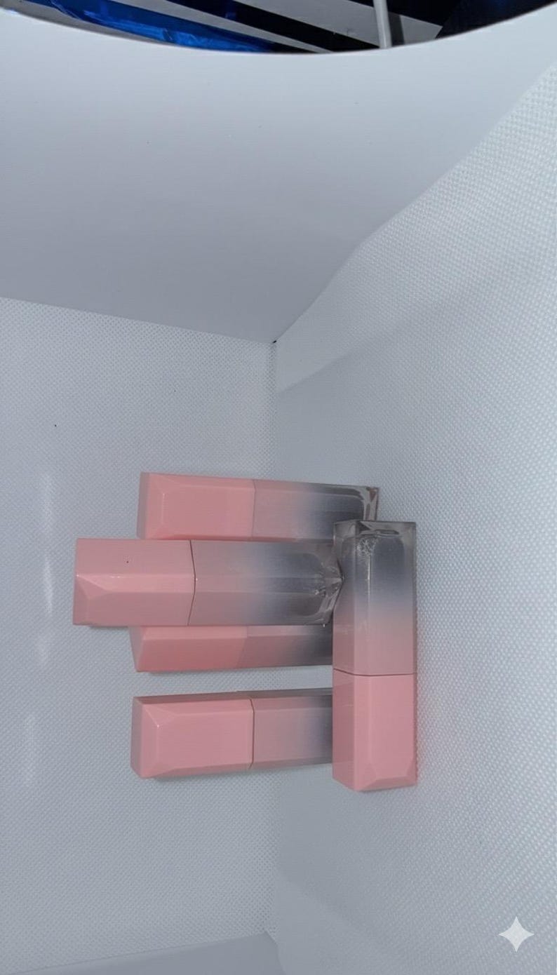 Puede incluir: Una colecci&oacute;n de labiales rosas y transparentes. Los labiales tienen un dise&ntilde;o degradado, que pasa del rosa al transparente. Los tubos de l&aacute;piz labial est&aacute;n dispuestos verticalmente, mostrando su forma y color.