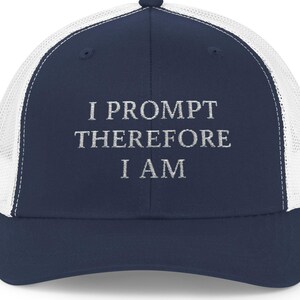 May include: A navy blue and white trucker cap with the text "I PROMPT THEREFORE I AM" embroidered in white. The cap has a curved peak and a mesh back for ventilation.