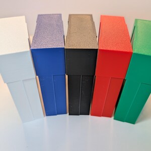 May include: Five rectangular plastic storage cases standing upright in a row. The cases are colored white, blue, black, red, and green from left to right. Each case features a smooth, solid-colored exterior with a distinct lid and base section.