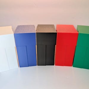 May include: A set of five rectangular storage boxes arranged in a row, featuring a white, blue, black, red, and green box. Each box has a two-part design with a lid and a base, displaying a smooth, solid-colored finish and vertical structural lines.