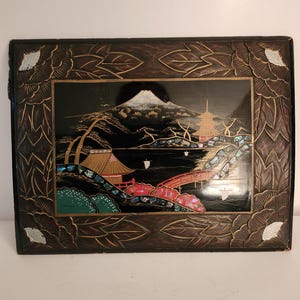 Può includere: Vassoio rettangolare in lacca nera con una scena di paesaggio giapponese. La scena presenta una montagna innevata, una pagoda e un ponte rosso. Il vassoio è incorniciato con disegni floreali e di foglie intagliate.