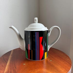 May include: A white ceramic mug with a black handle and the text "But First, Coffee" in a black, bold font. The mug is sitting on a white surface. The mug is approximately 4 inches tall.