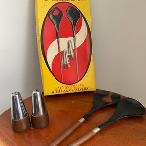 Può includere: Un set da insalata vintage con una scatola gialla con la scritta "Modern Style Salad Set". Il set include posate da insalata nere con manici in legno, due saliere e pepiere con coperchi argentati.