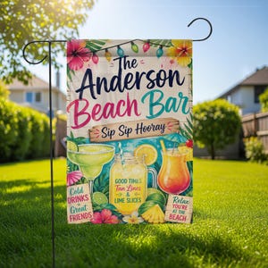 May include: A garden flag with the text "The Anderson Beach Bar" and illustrations of cocktails, limes, and tropical flowers. The flag also includes the phrases "Sip Sip Hooray", "Cold Drinks & Great Friends", "Good Times, Tan Lines & Lime Slices", and "Relax You're at the Beach".