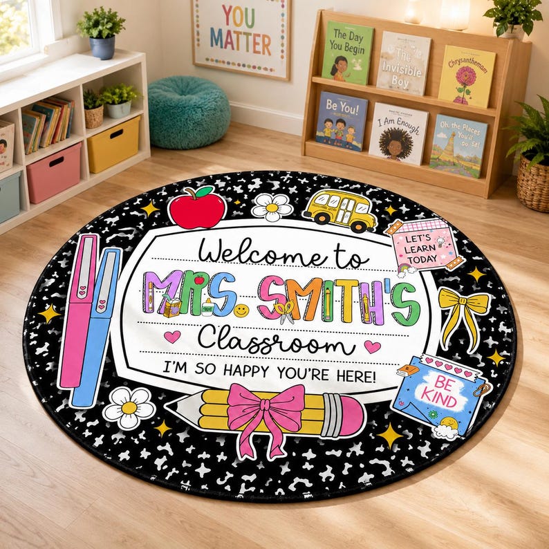 May include: A round classroom rug with a black and white speckled background. The center features a white sign with the text "Welcome to MRS. SMITH'S Classroom I'M SO HAPPY YOU'RE HERE!" decorated with a red apple, yellow bus, pencil, and bow.