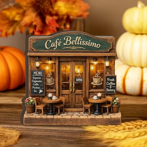 May include: A miniature wooden cafe with the text "Café Bellissimo" above the entrance. The cafe has a detailed facade with a menu, tables, chairs, and the words "Fresh Coffee & Bakery". The scene is warmly lit.