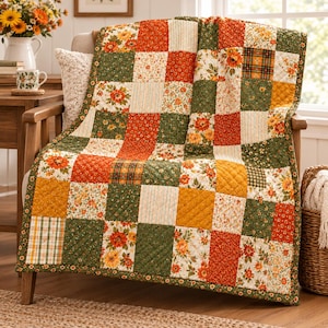 Op de afbeelding: Een patchwork quilt met een raster van vierkante stoffen panelen in tinten oranje, mosterdgeel en bosgroen. De quilt toont een verscheidenheid aan patronen, waaronder bloemenprints, dunne strepen en ruitontwerpen met een ruitvormig stiksel.