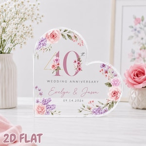 Può includere: Una targa in acrilico trasparente a forma di cuore con un motivo floreale di rose rosa e fiori viola. Il testo recita 40th WEDDING ANNIVERSARY, Evelyn & Jason e 14.09.2026. Il design include foglie verdi e un accento a triangolo dorato.
