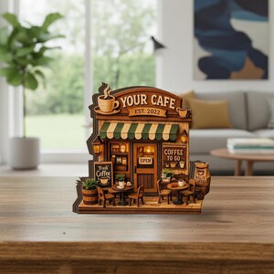 May include: A wooden model of a cafe, featuring the text "YOUR CAFE EST. 2022". The cafe has a green and white striped awning, a sign that says "Fresh Coffee", and small tables and chairs. The cafe is brown with a light brown trim.