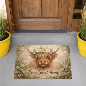 May include: A rectangular doormat featuring a Highland cow with a floral crown and the text "Home Sweet Home." The mat has a light brown background with a border of flowers and greenery. The cow is depicted in shades of brown and tan.