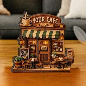 May include: A detailed wooden model of a cafe, featuring the text "YOUR CAFE EST. 2022". It has a green and white striped awning, small tables, chairs, and a sign that reads "COFFEE TO GO". A small sign reads "Fresh Coffee".