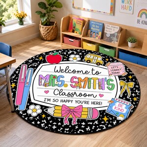 May include: A round classroom rug with a black and white speckled background. The center features a white sign with the text "Welcome to MRS. SMITH'S Classroom I'M SO HAPPY YOU'RE HERE!" surrounded by illustrations of a red apple, school bus, pencil, and bow.