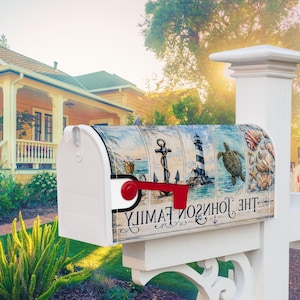 May include: A white metal mailbox featuring a nautical-themed wrap with illustrations of a bicycle, an anchor, a lighthouse, a sea turtle, and seashells. The text THE JOHNSON FAMILY is printed in black script across the bottom of the design.