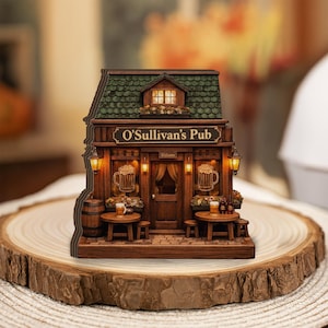 May include: A miniature wooden replica of O'Sullivan's Pub. The pub features a green shingled roof, a sign that reads "O'Sullivan's Pub", and two beer mugs on the front. The pub has two small tables with stools and a barrel.