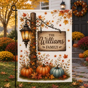 Puede incluir: Una bandera de jardín rectangular con un poste de madera, una linterna colgante y un letrero que dice THE Williams FAMILY. La escena incluye calabazas naranjas y azules en la base, rodeadas de hojas de otoño sobre un fondo color crema.