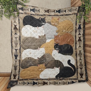 Op de afbeelding: Een beige quilt met een patroon van slapende katten in verschillende kleuren, waaronder zwart, wit, grijs en oranje. De quilt heeft een visgraatrandontwerp. De katten zijn gerangschikt in een gestapeld, gelaagd ontwerp.