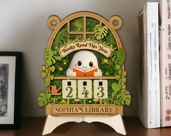 May include: Wooden bookshelf decor with a cute ghost reading a book. The sign reads "Books Read This Year" and "Sophia's Library." The counter shows "243" books read. Green leaves and vines surround the ghost and the counter.