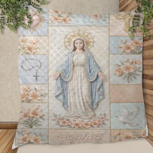 May include: A quilted blanket featuring a central image of a religious figure with a halo, surrounded by floral and religious symbols. The color palette includes soft blues, pinks, and creams. The name "Sophia" is embroidered at the bottom.