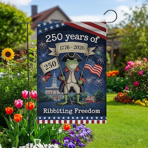 Puede incluir: Una bandera de jardín con un personaje de rana patriótica sosteniendo banderas americanas. La bandera dice "250 años de 1776-2026" y "Ribbiting Freedom" con un diseño de fuegos artificiales y el edificio del Capitolio de los Estados Unidos. La bandera está en un jardín.