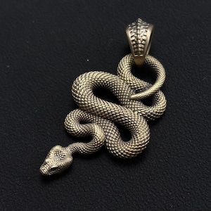 May include: A detailed pendant in the shape of a snake, crafted from a metallic material with a textured, scale-like pattern. The snake is coiled, with its head raised, and has a loop at the top for a chain. The pendant is a bronze color.