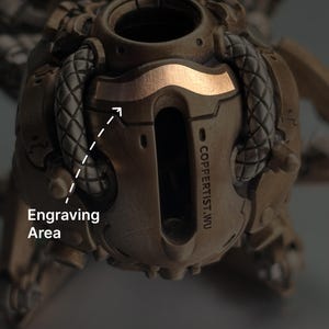 May include: Close-up of a bronze-colored, mechanical-looking object with a copper-colored accent. The text "COPPERTIST.WU" is visible. The image highlights an engraving area.