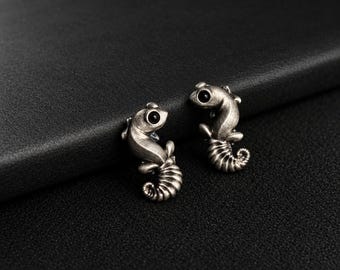 May include: A pair of stud earrings shaped like seahorses with an antiqued silver finish and small black circular stones for eyes. The seahorse figures feature detailed curved tails and textured bodies, crafted in a metallic material.