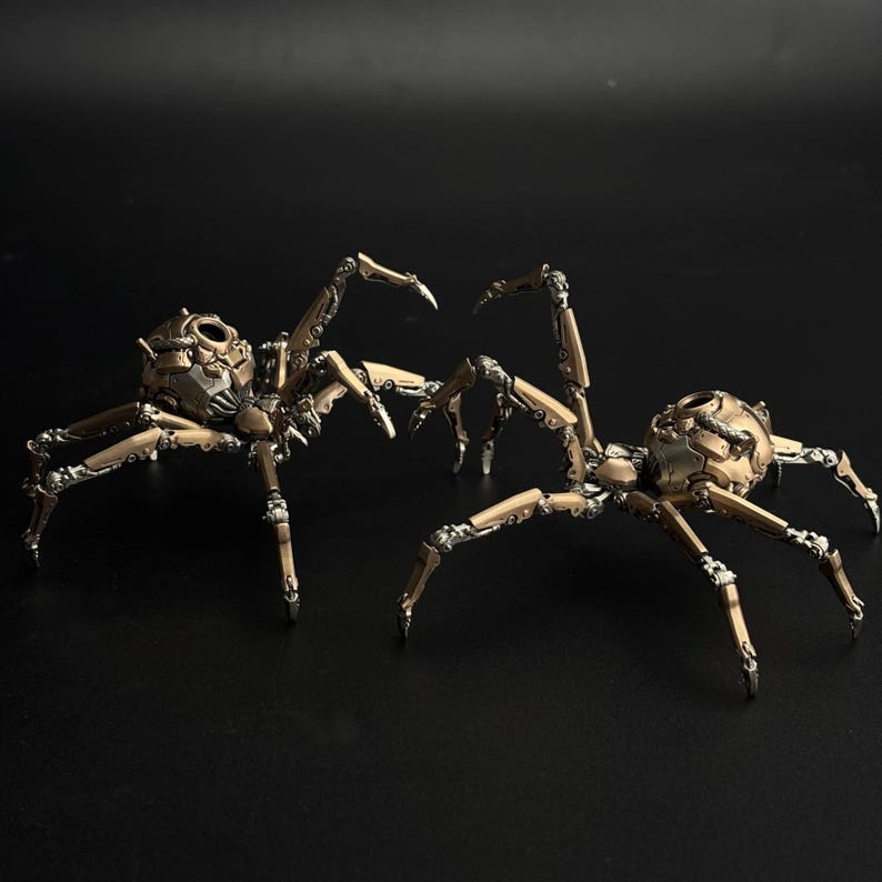 May include: Two steampunk-style spider sculptures. The spiders are bronze and silver in color, with intricate mechanical details. Each spider has a rounded head and multiple articulated legs. The sculptures are set against a black background.