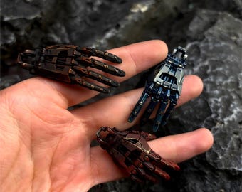 May include: Three miniature robotic hands in bronze, blue, and copper tones. Each hand features intricate mechanical details, including articulated fingers and a metallic finish. The hands are designed with a futuristic aesthetic.