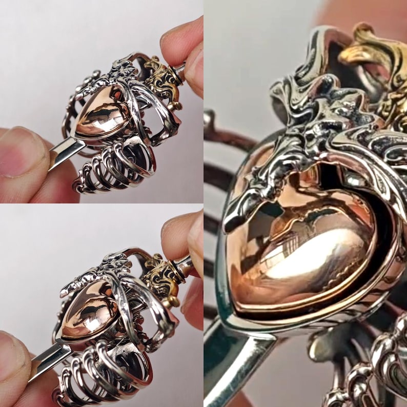 Op de afbeelding: Een metalen haaraccessoire met een gepolijst ros&eacute;gouden hart in het midden, ingesloten in een gedetailleerde zilverkleurige kooistructuur die lijkt op een borstkas. Het ontwerp bevat ingewikkelde, vloeiende metaalbewerking en een gladde afwerking.