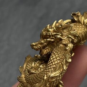 May include: A detailed, golden dragon figurine. The dragon is sculpted with intricate scales, a flowing mane, and a fierce expression. The figurine is made of a shiny, metallic material, and the dragon is posed in a dynamic, powerful stance.