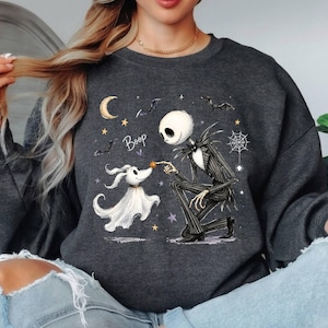 May include: A dark gray crewneck sweatshirt featuring a graphic of a skeletal figure in a pinstripe suit kneeling before a ghost dog. The design includes the text Boop, a crescent moon, stars, bats, and a spiderweb in white, yellow, and purple tones.