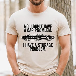 May include: Beige t-shirt with the text "NO, I DON'T HAVE A CAR PROBLEM. I HAVE A STORAGE PROBLEM." in black. Below the text are four black car silhouettes.