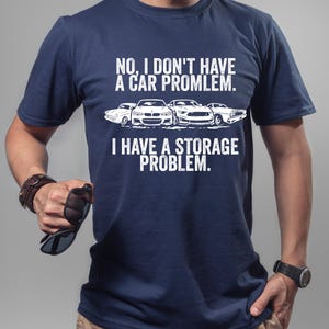 May include: Navy blue t-shirt with the text "NO, I DON'T HAVE A CAR PROMLEM. I HAVE A STORAGE PROBLEM." and a graphic of four cars in white. The shirt is made of a soft material.