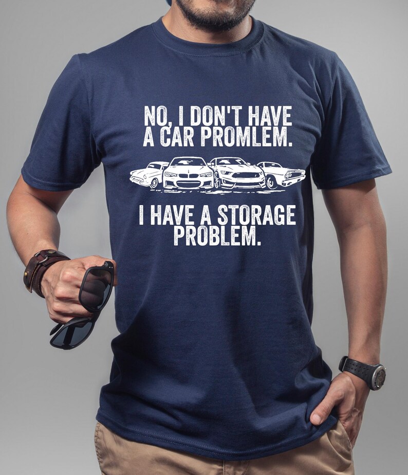 May include: Navy blue t-shirt with the text "NO, I DON'T HAVE A CAR PROMLEM. I HAVE A STORAGE PROBLEM." and a graphic of four cars in white. The shirt is made of a soft material.