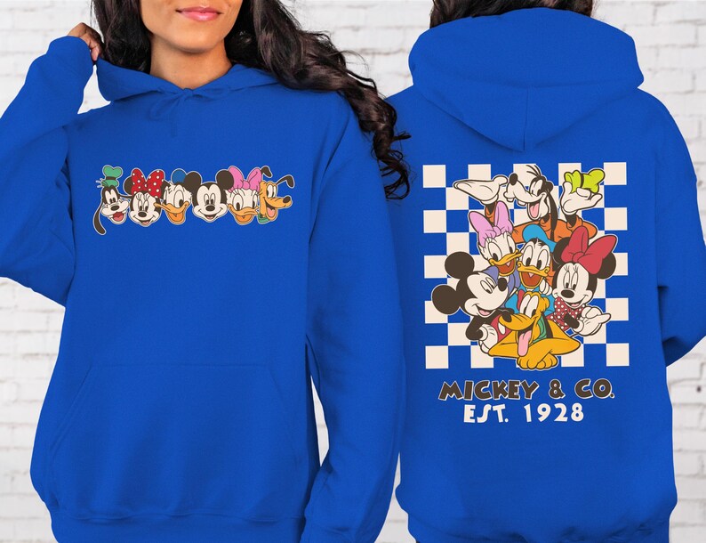 Puede incluir: Sudadera con capucha azul real con un dise&ntilde;o de personajes de Disney. La parte delantera muestra caras de personajes, mientras que la parte trasera muestra un grupo de personajes sobre un fondo a cuadros con "Mickey & Co. Est. 1928".