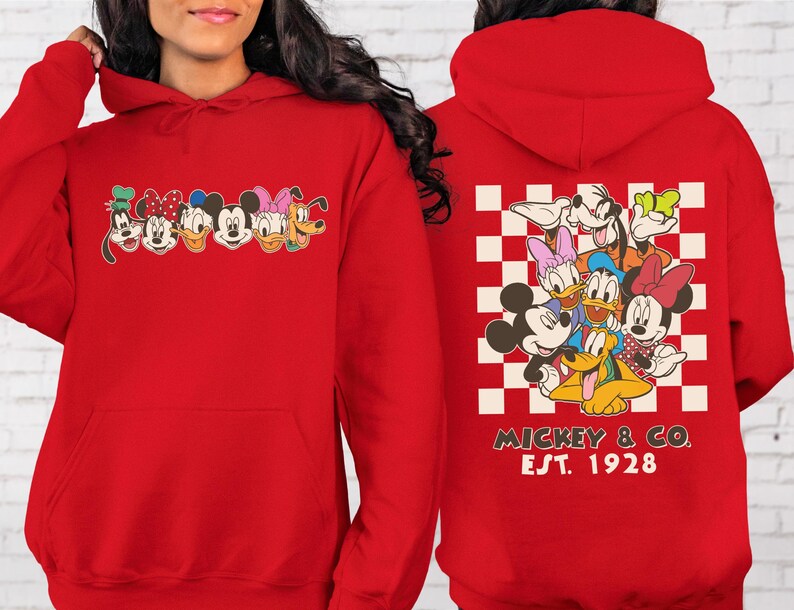 Puede incluir: Sudadera con capucha roja con un gr&aacute;fico de personajes de Disney en la parte delantera y trasera. La parte delantera muestra a Goofy, Minnie, Mickey, Daisy y Pluto. La parte trasera tiene un patr&oacute;n de cuadros con los personajes y el texto "Mickey & Co. Est. 1928."