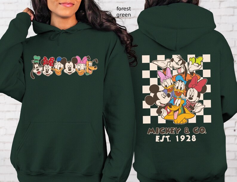 Puede incluir: Sudadera con capucha verde bosque con un gr&aacute;fico de dibujos animados de Mickey Mouse, Minnie Mouse, Donald Duck, Daisy Duck, Goofy y Pluto. La parte trasera tiene un patr&oacute;n de cuadros con los personajes y el texto "Mickey & Co. Est. 1928".