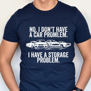 May include: Navy blue t-shirt with white text and car graphics. The text reads "NO, I DON'T HAVE A CAR PROBLEM. I HAVE A STORAGE PROBLEM."