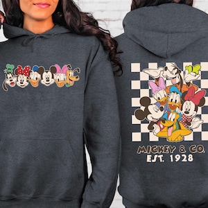 Puede incluir: Sudadera con capucha gris oscuro con un gr&aacute;fico colorido de personajes de dibujos animados en el pecho y la espalda. El gr&aacute;fico frontal incluye a Mickey Mouse, Minnie Mouse, Donald Duck, Daisy Duck, Goofy y Pluto. El gr&aacute;fico trasero est&aacute; sobre un fondo a cuadros con el texto "Mickey & Co. Est. 1928."