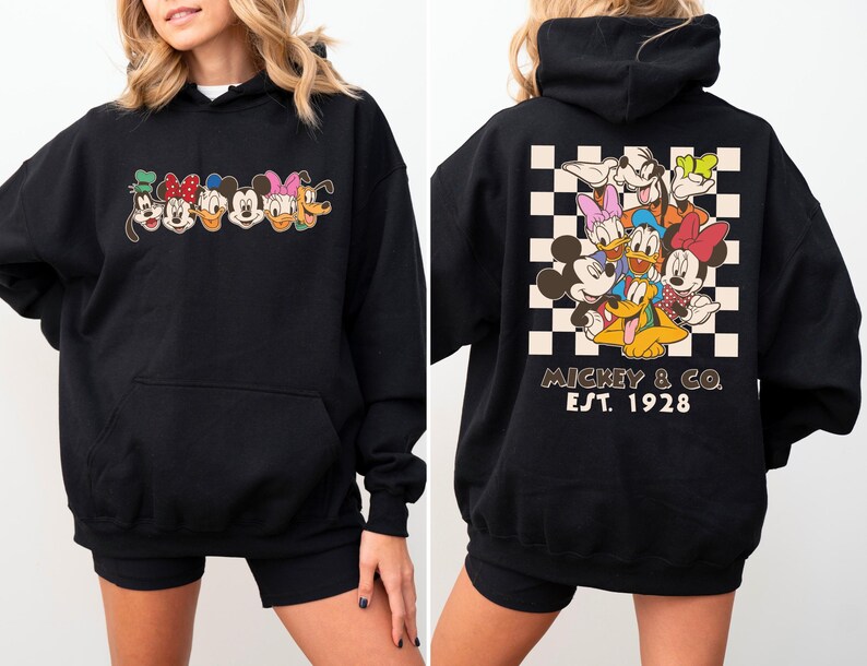 Puede incluir: Sudadera con capucha negra con un dise&ntilde;o de personajes de Disney. La parte delantera muestra caras de personajes, mientras que la parte trasera presenta un grupo de personajes sobre un fondo a cuadros con "Mickey & Co. Est. 1928".