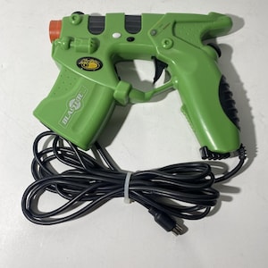 Può includere: Un controller a pistola luminosa per videogiochi in plastica verde con un grilletto nero e un cavo nero. La pistola ha la scritta "Blaster" stampata sul lato. La canna è arancione. Il cavo è legato con una fascetta bianca.