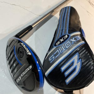 Puede incluir: Un palo de golf EXOTICS EXS negro y azul con una funda a juego. La funda es negra con detalles azules y plateados y el logotipo EXS. El palo tiene una varilla plateada.